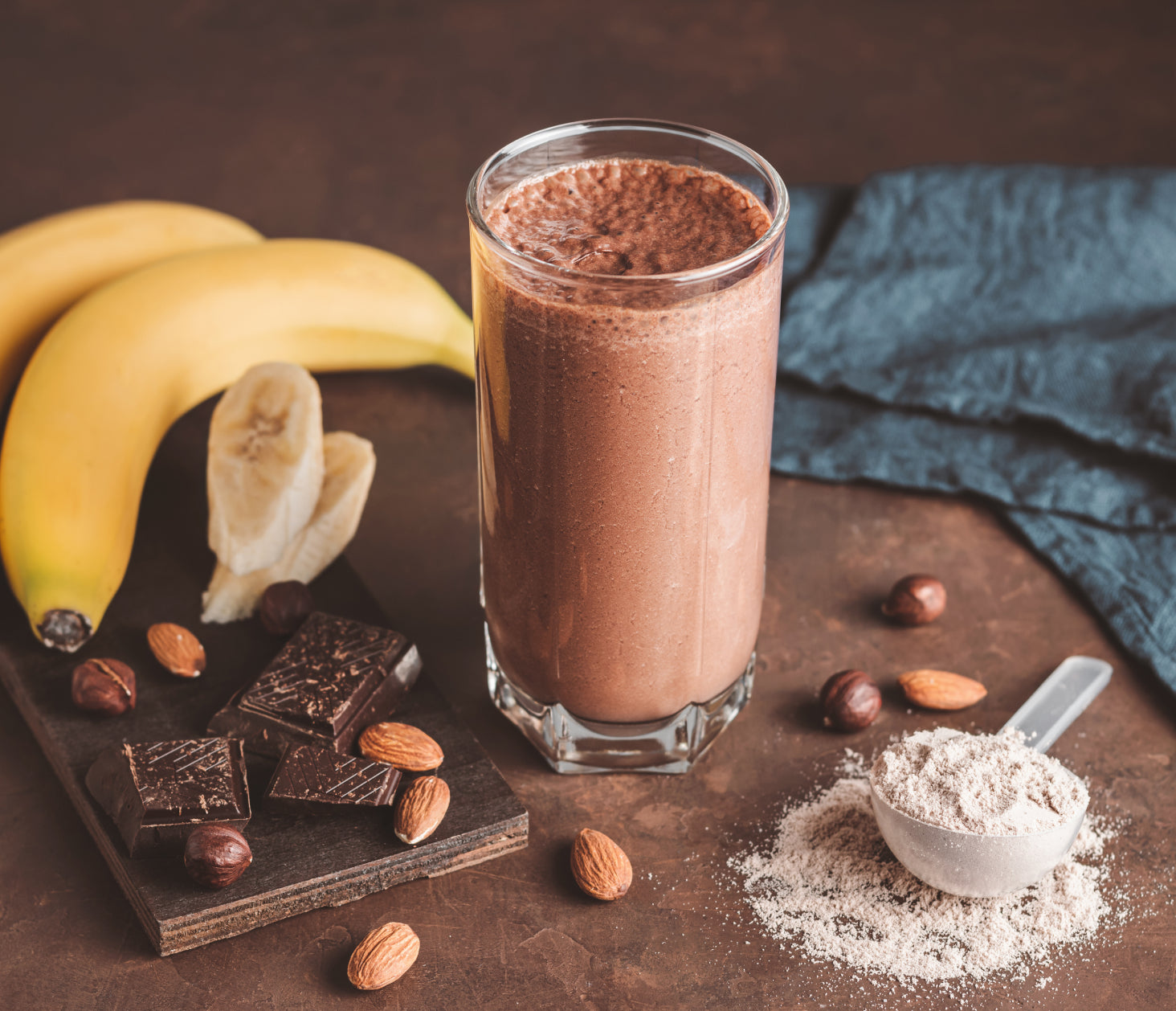 Chocolate Protein Shake with bananas, chocolate and protein powder next to it.