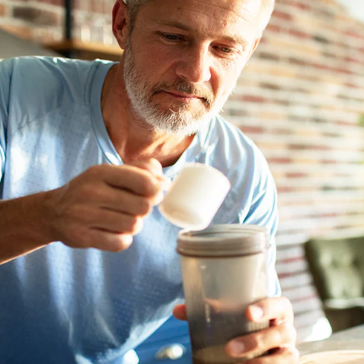 Man in a blue shirt holding a container and a spoon preparing a drink.