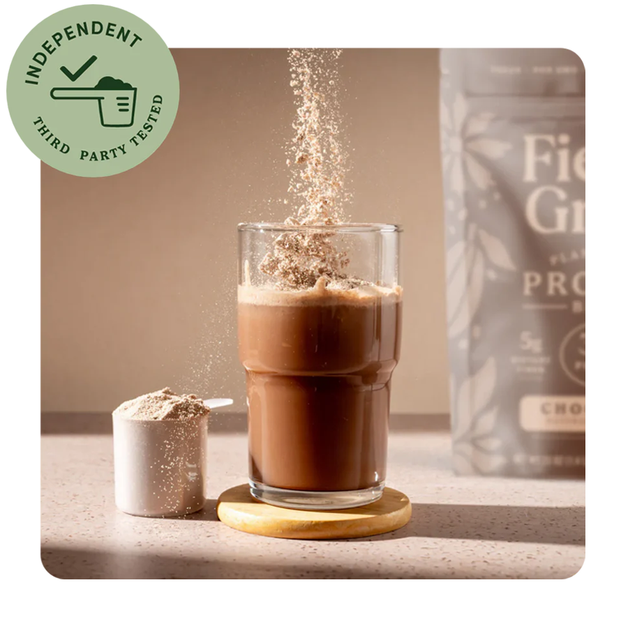 Glass of chocolate drink with a scoop of protein powder and a container of protein powder on a neutral background.