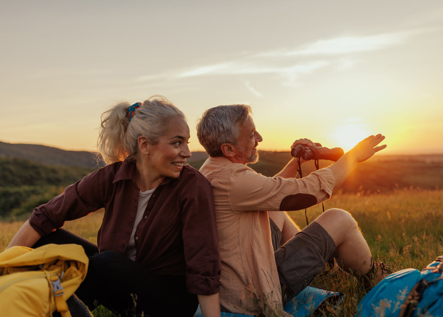 Middle-aged man and woman sitting in field at sunset.